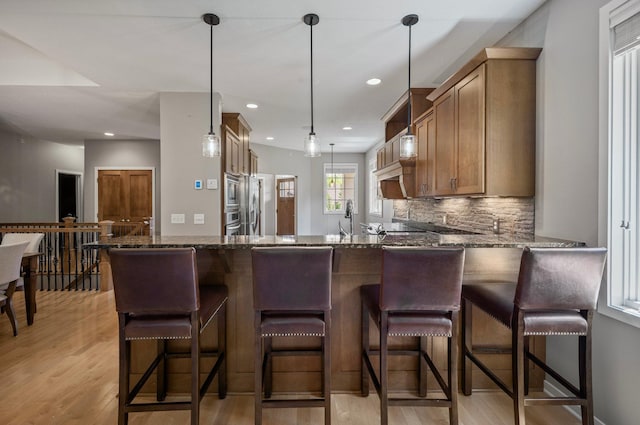17365 Hanson Ct, Eden Prairie, MN 55347 - kitchen featuring light wood-style floors, dark stone countertops, backsplash, a peninsula, and decorative light fixtures