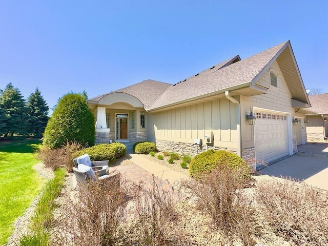 17365 Hanson Ct, Eden Prairie, MN 55347 - view of front facade featuring an attached garage, stone siding, a shingled roof, concrete driveway, and board and batten siding