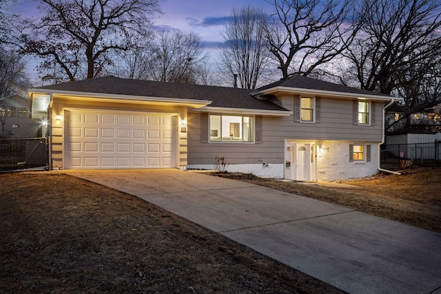 tri-level home with brick siding, an attached garage, driveway, and fence