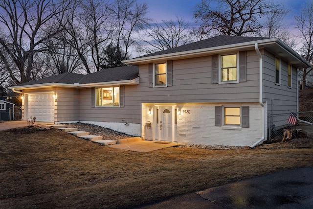 split level home with brick siding, an attached garage, roof with shingles, and fence