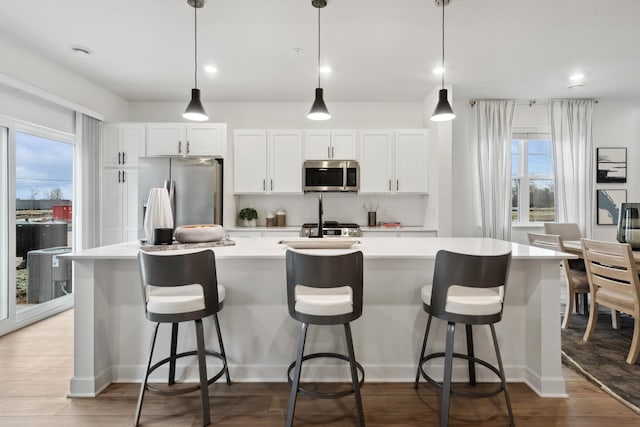 kitchen featuring appliances with stainless steel finishes, decorative light fixtures, an island with sink, and white cabinets