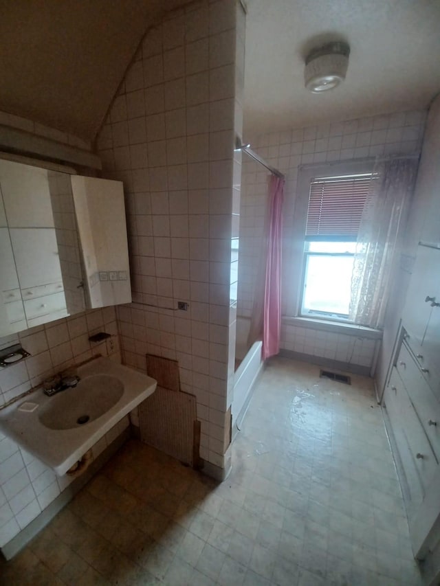 bathroom with radiator heating unit, sink, shower / bath combo with shower curtain, and tile walls