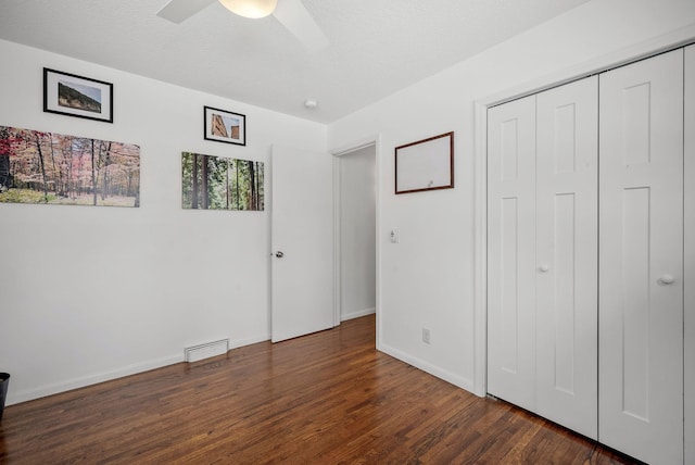 unfurnished bedroom with a textured ceiling, dark wood-style flooring, visible vents, baseboards, and a closet