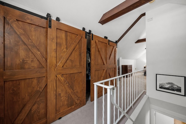 corridor with lofted ceiling, a barn door, light colored carpet, and an upstairs landing