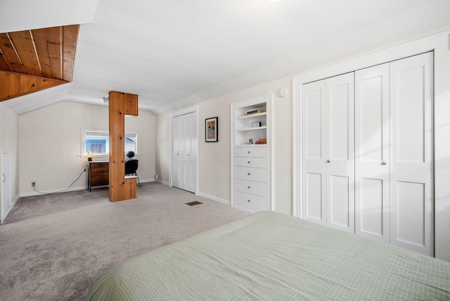 carpeted bedroom featuring vaulted ceiling and multiple closets