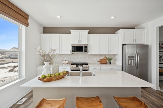 kitchen featuring stainless steel appliances, white cabinetry, an island with sink, and a kitchen bar