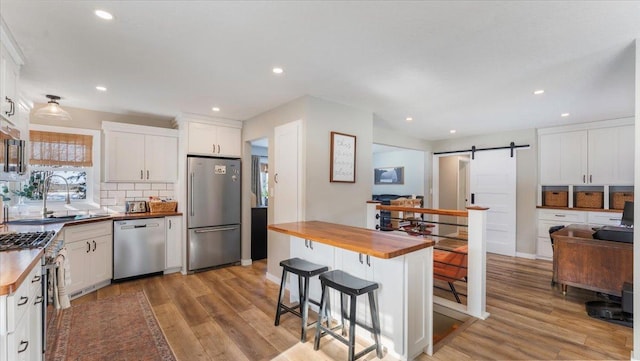 kitchen featuring butcher block counters, tasteful backsplash, stainless steel appliances, a barn door, and white cabinets