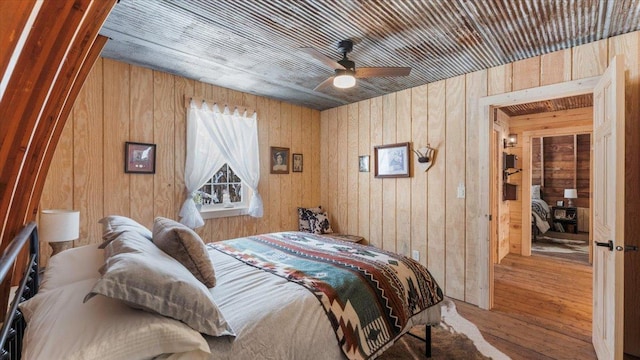 bedroom with hardwood / wood-style floors, ceiling fan, and wood walls