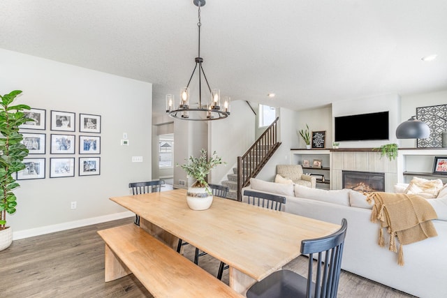 dining area featuring a tiled fireplace, a textured ceiling, wood-type flooring, and a chandelier