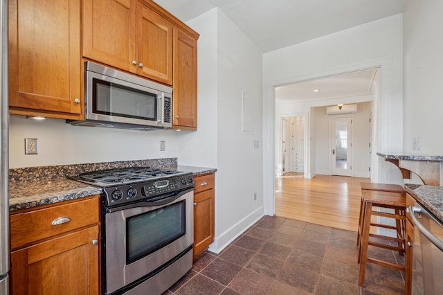 kitchen with baseboards, brown cabinetry, dark stone counters, a wall unit AC, and stainless steel appliances