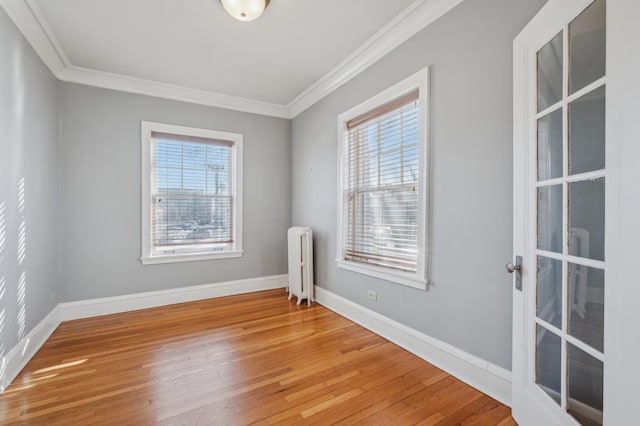 spare room with crown molding, wood finished floors, and radiator