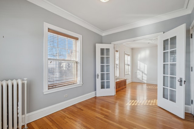 spare room featuring baseboards, radiator heating unit, light wood-style flooring, ornamental molding, and french doors