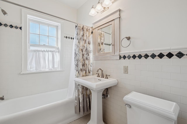 full bath with tile walls, wainscoting, toilet, shower / bathtub combination with curtain, and a sink