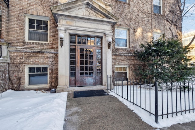 snow covered property entrance with fence and brick siding