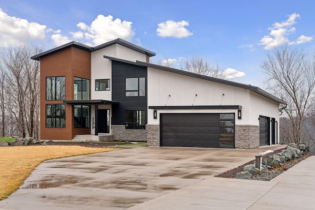 contemporary home with a garage, stone siding, driveway, and stucco siding