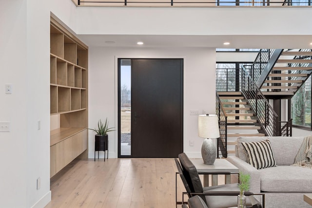 entryway featuring light wood finished floors, baseboards, a high ceiling, and stairway