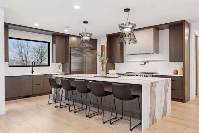 kitchen featuring wall chimney exhaust hood, modern cabinets, a center island, stainless steel appliances, and light wood-type flooring