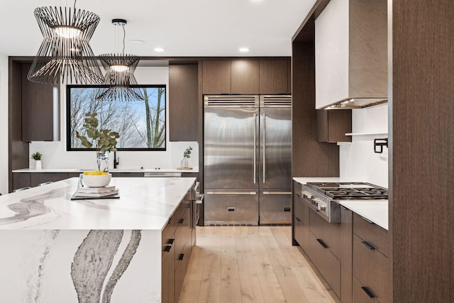 kitchen featuring dark brown cabinetry, light wood finished floors, modern cabinets, custom exhaust hood, and stainless steel appliances