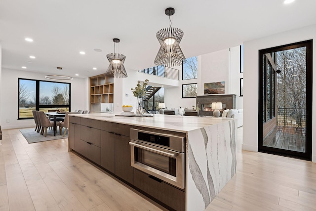 kitchen with light wood finished floors, modern cabinets, open floor plan, hanging light fixtures, and stainless steel oven