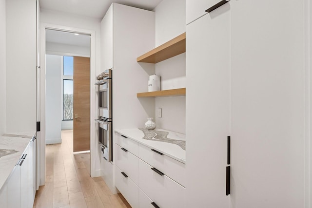 kitchen with white cabinets, light wood-style flooring, modern cabinets, light stone counters, and stainless steel double oven