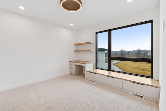 spare room featuring baseboards, visible vents, built in desk, and carpet flooring