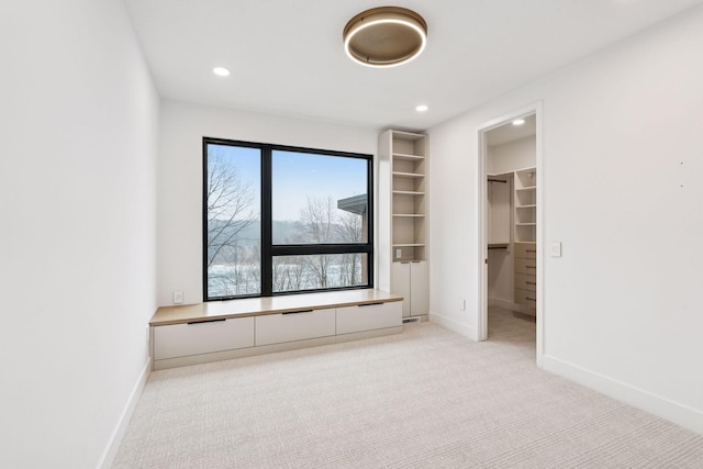 unfurnished bedroom featuring recessed lighting, baseboards, a walk in closet, and light colored carpet