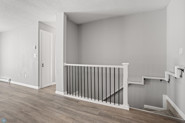 stairs featuring hardwood / wood-style flooring, a baseboard radiator, and a textured ceiling