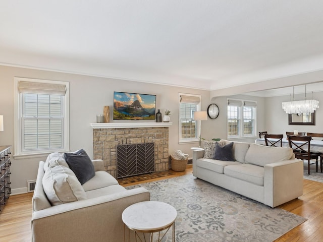 living area featuring light wood-style flooring, baseboards, visible vents, a fireplace, and a notable chandelier