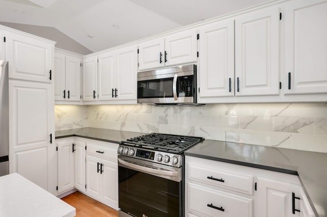 kitchen with light wood-type flooring, stainless steel appliances, vaulted ceiling, white cabinetry, and tasteful backsplash