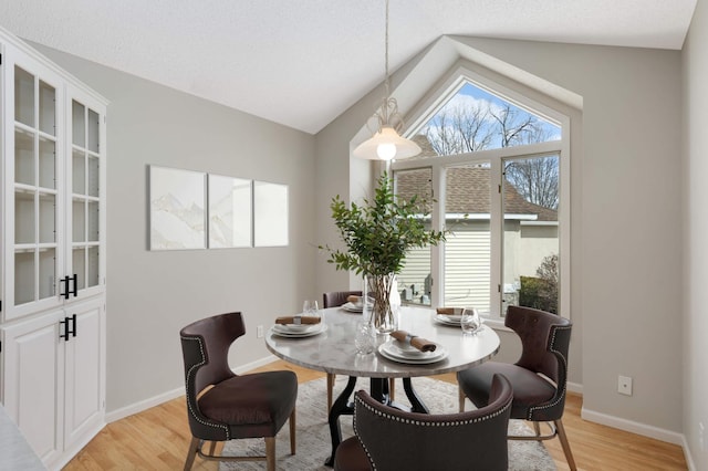 dining room with a textured ceiling, baseboards, light wood-style floors, and vaulted ceiling