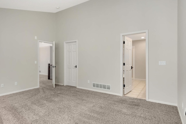 unfurnished bedroom featuring light carpet, visible vents, high vaulted ceiling, and baseboards