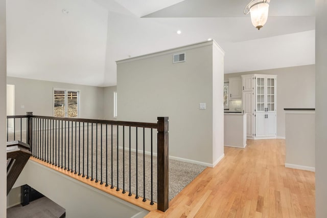 corridor with lofted ceiling, an upstairs landing, visible vents, and baseboards