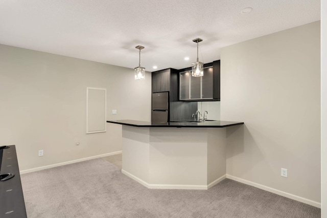 kitchen featuring dark countertops, baseboards, light colored carpet, a peninsula, and freestanding refrigerator