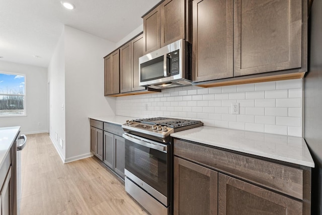 kitchen featuring light wood-style flooring, dark brown cabinetry, light countertops, appliances with stainless steel finishes, and tasteful backsplash