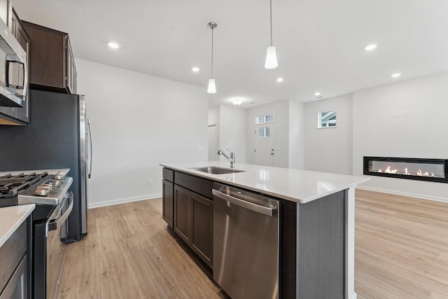 kitchen with a sink, a glass covered fireplace, appliances with stainless steel finishes, light wood finished floors, and dark brown cabinets