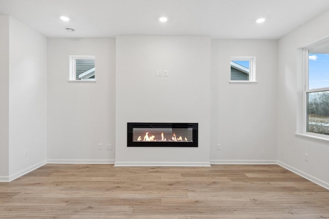 unfurnished living room featuring a glass covered fireplace, recessed lighting, baseboards, and light wood finished floors