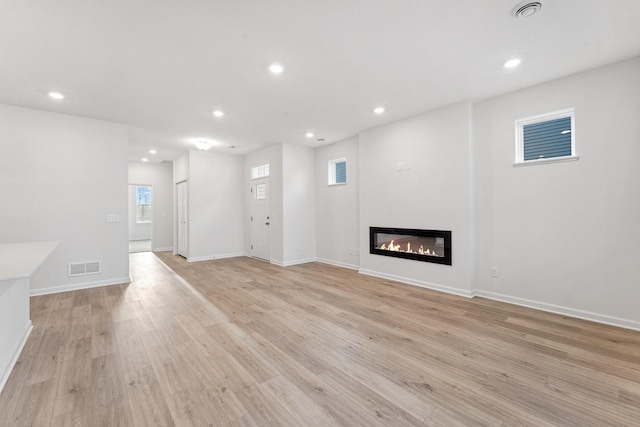 unfurnished living room featuring recessed lighting, light wood-type flooring, visible vents, and a glass covered fireplace