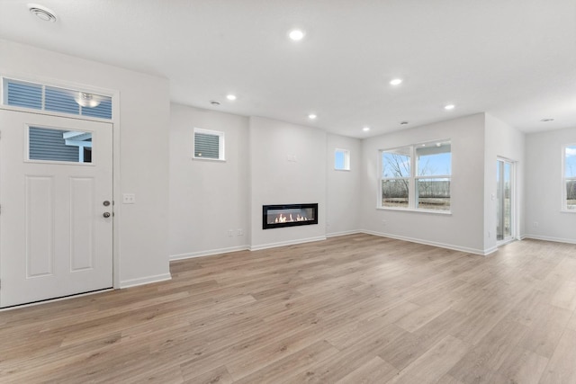 unfurnished living room with a glass covered fireplace, recessed lighting, light wood-type flooring, and a wealth of natural light