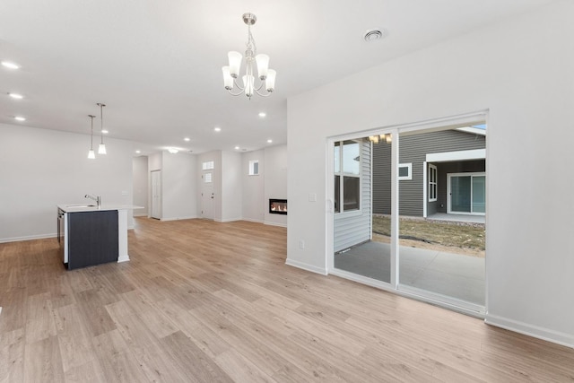 unfurnished living room with a sink, a glass covered fireplace, recessed lighting, light wood finished floors, and baseboards