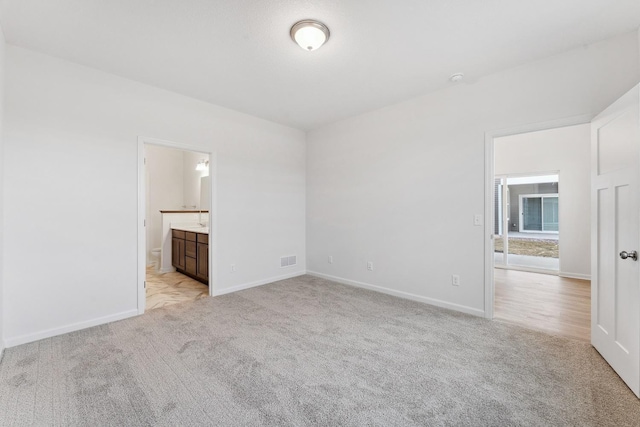 unfurnished bedroom featuring visible vents, light colored carpet, ensuite bathroom, and baseboards