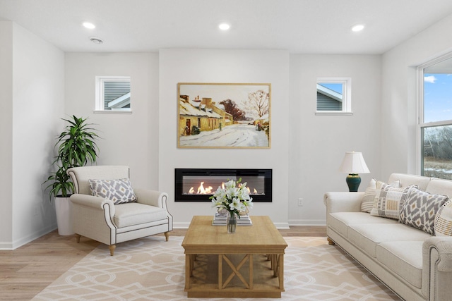 interior space featuring a glass covered fireplace, recessed lighting, light wood-type flooring, and baseboards