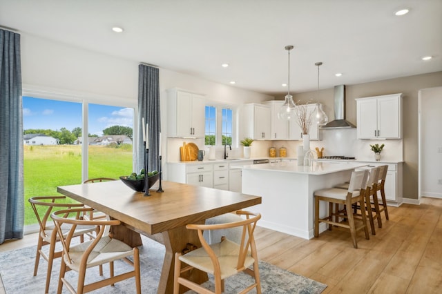 kitchen with pendant lighting, wall chimney exhaust hood, a kitchen island, and white cabinets