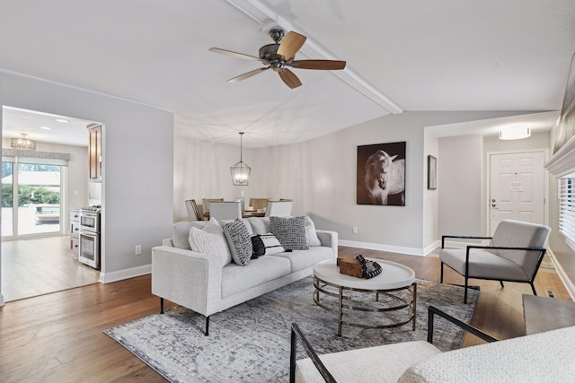 living room featuring lofted ceiling with beams, ceiling fan with notable chandelier, and hardwood / wood-style floors