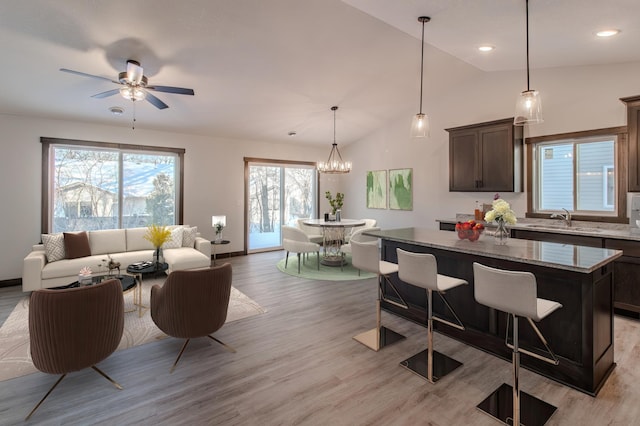 kitchen featuring sink, a breakfast bar, dark brown cabinets, a center island, and light stone countertops