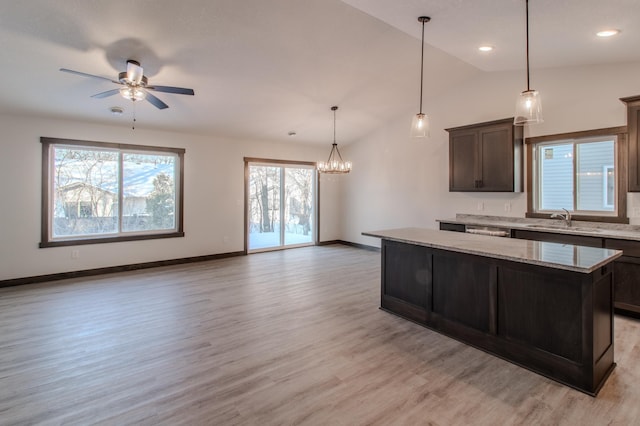 kitchen featuring sink, dark brown cabinets, a center island, light stone counters, and light hardwood / wood-style floors