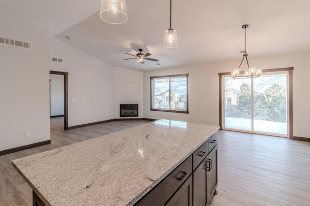 kitchen with lofted ceiling, light stone counters, decorative light fixtures, light wood-type flooring, and a fireplace