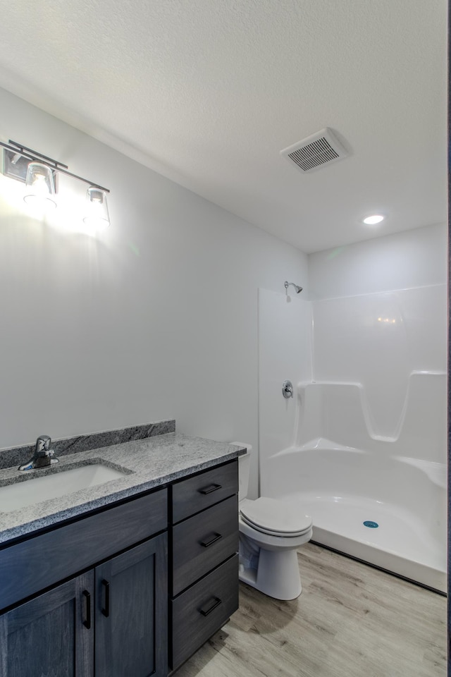 bathroom featuring vanity, wood-type flooring, a textured ceiling, toilet, and walk in shower