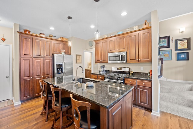 kitchen with a breakfast bar, an island with sink, a sink, stainless steel appliances, and light wood-style floors