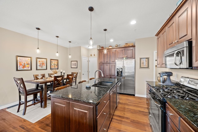 kitchen featuring dark stone countertops, wood finished floors, a sink, appliances with stainless steel finishes, and decorative light fixtures