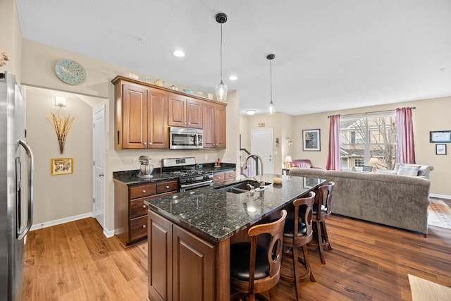 kitchen with light wood finished floors, open floor plan, a breakfast bar, stainless steel appliances, and a sink